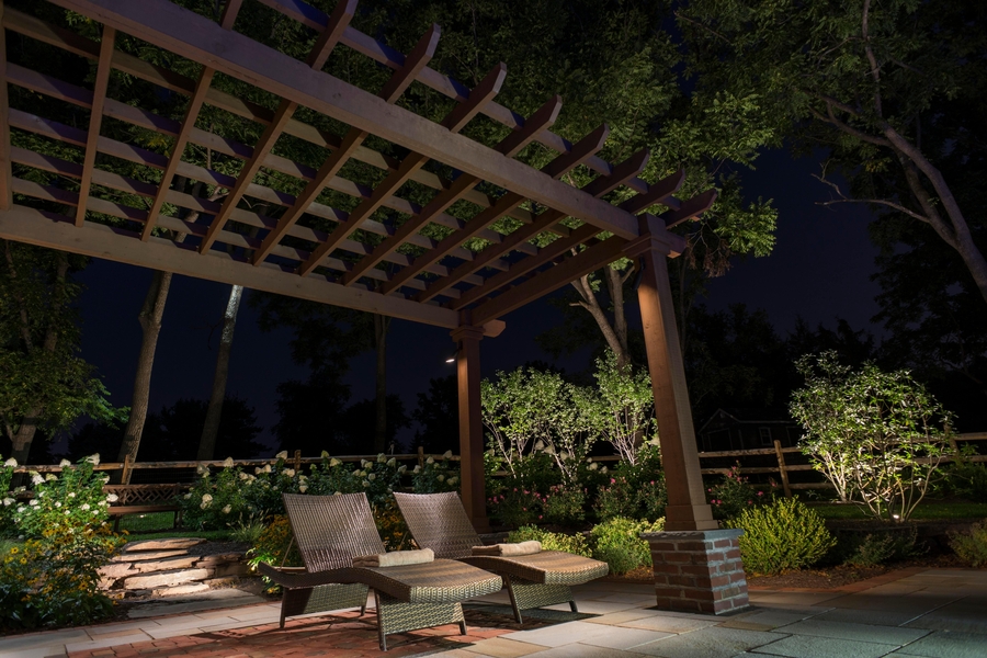 An upstate New York patio with a pergola, landscape lighting, and outdoor furniture.