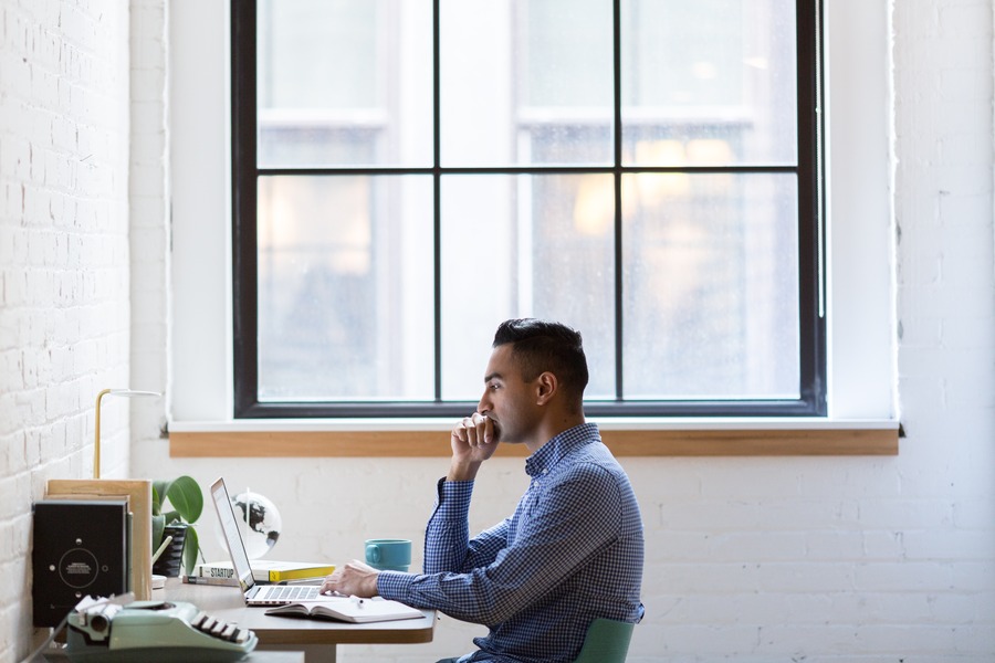 Man working at a desk on his computer next to a large window.