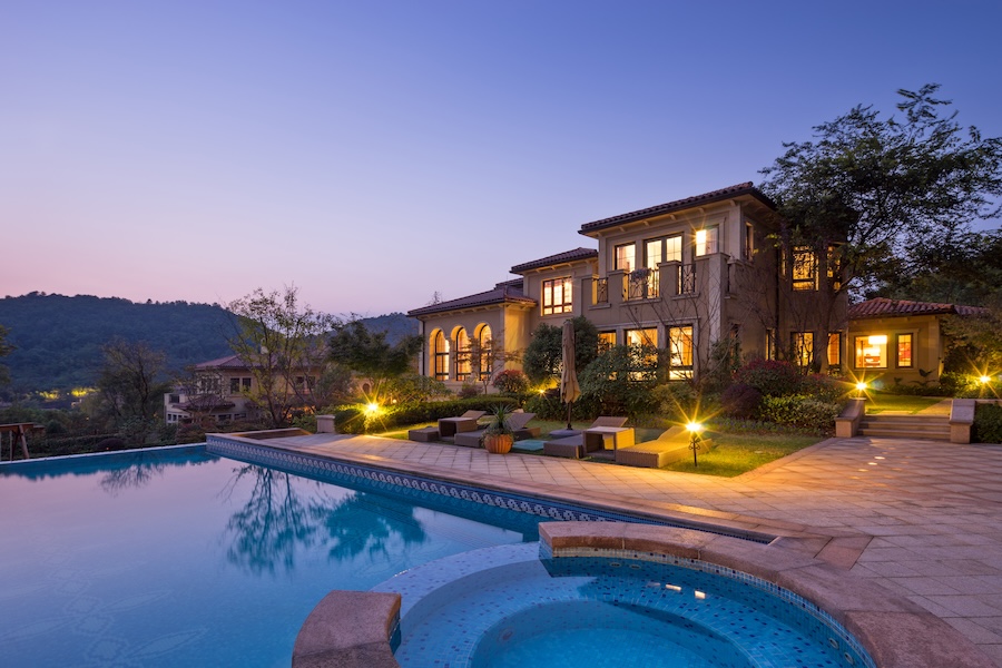 A pool in the evening near an illuminated home with pathway lighting in the landscape.