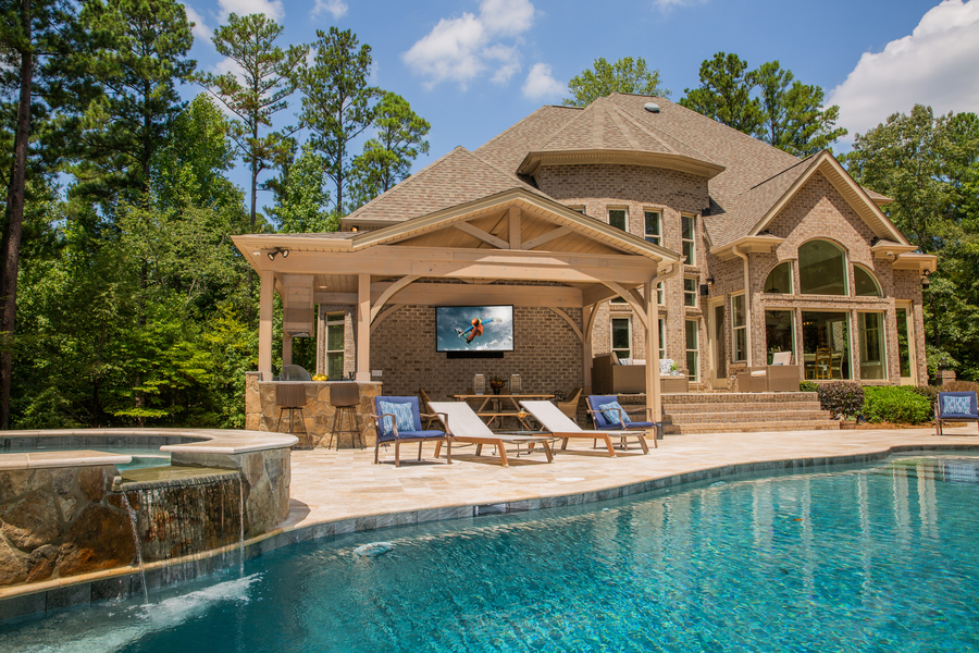A home’s backyard with a pool, spa, lounge chairs, and outdoor TV.